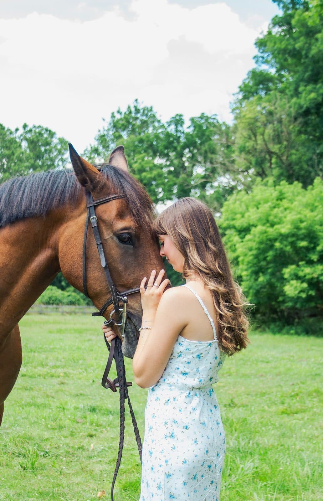 Aubrey Russo standing nose to nose with a bay horse in a green field
