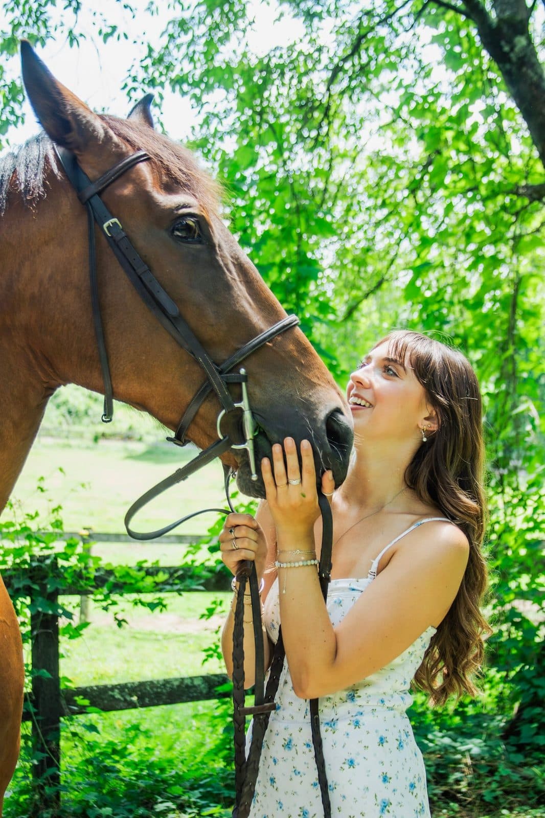 Aubrey Russo smiling up at a bay horse in a bridle beside a paddock fence